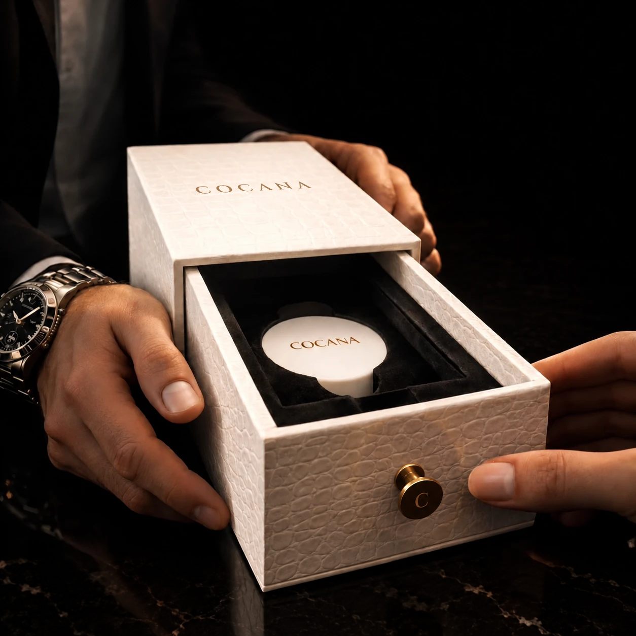 COCANA campaign visual: an open white textured case with a gold-tone C handle and black velvet interior.